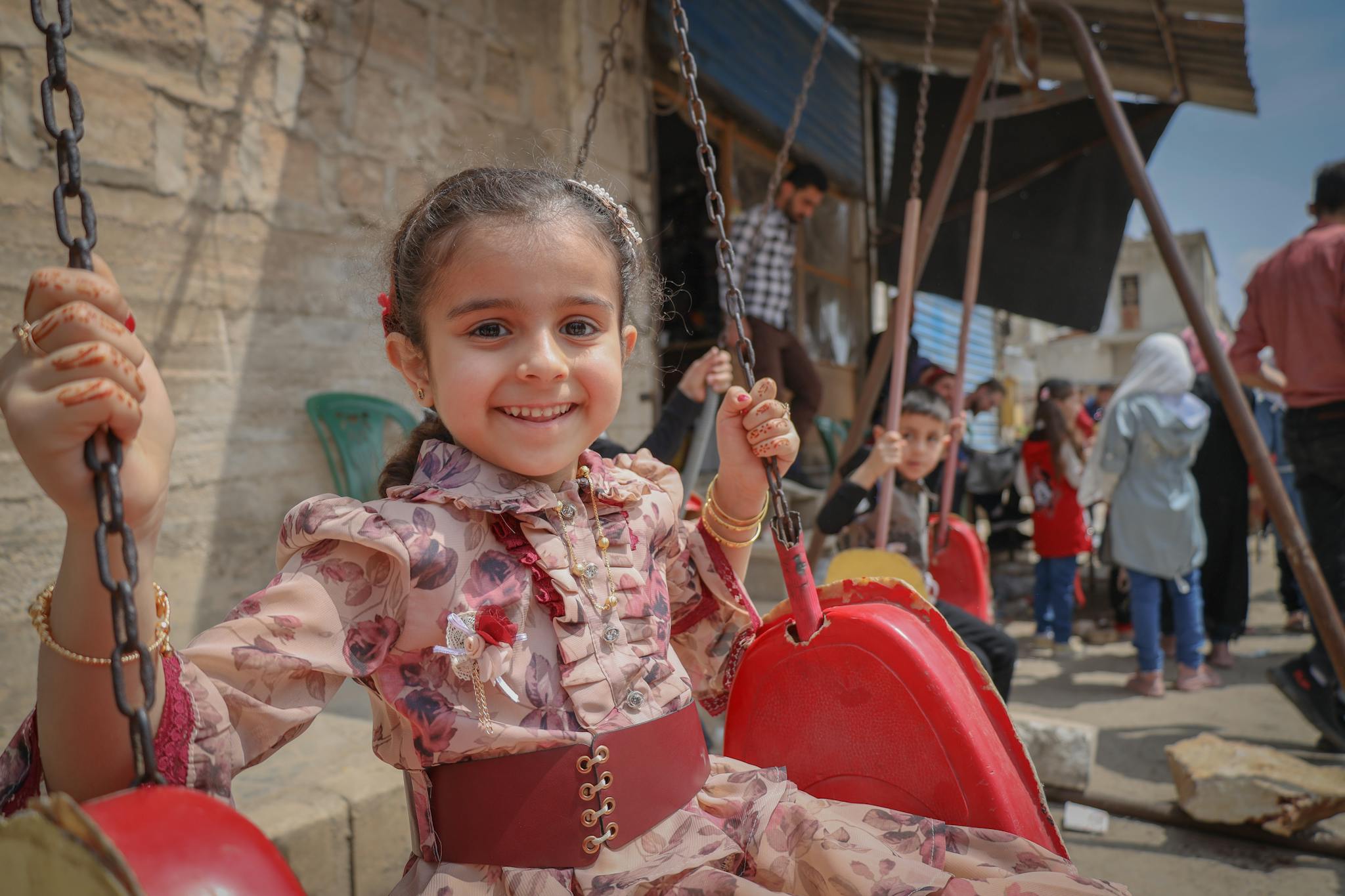 A cheerful young girl smiles while swinging outdoors in Idlib, Syria, capturing the innocence of childhood.
