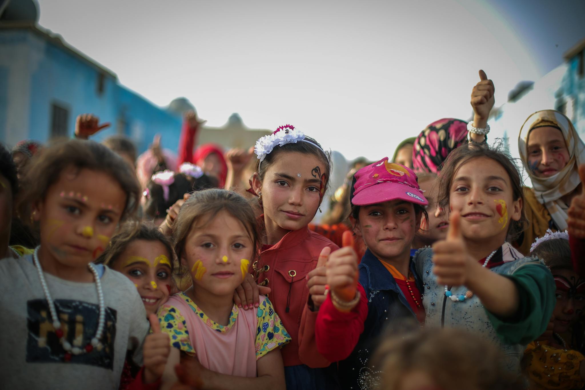 Happy group of children with face paint and thumbs up, enjoying outdoor festivities.